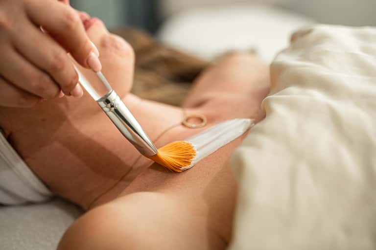 Close-up of spa treatment with person applying body paint using a gold-tipped brush