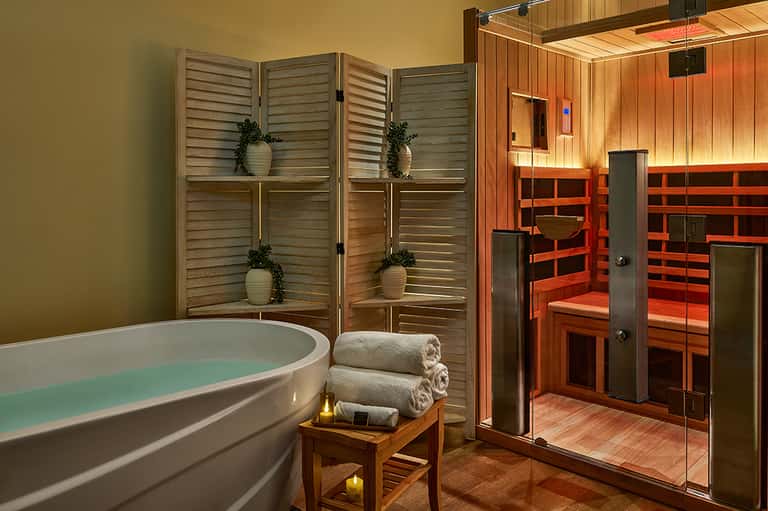 Spa wellness area with soaking tub, sauna, wooden screens, rolled towels, and soft lighting