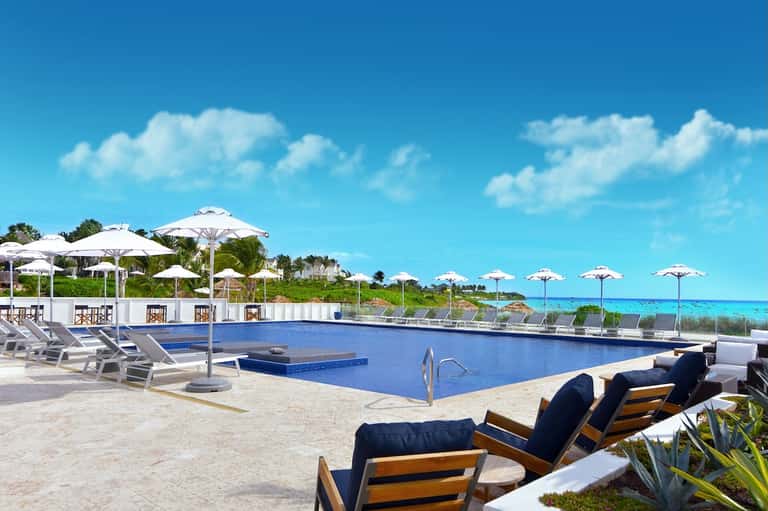 Oceanfront pool with white umbrellas, lounge chairs, and pristine turquoise water and beach