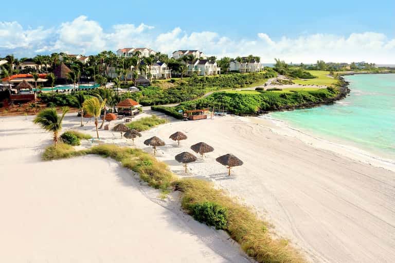 Beachfront resort with white buildings, palm trees, sand beach, and turquoise water