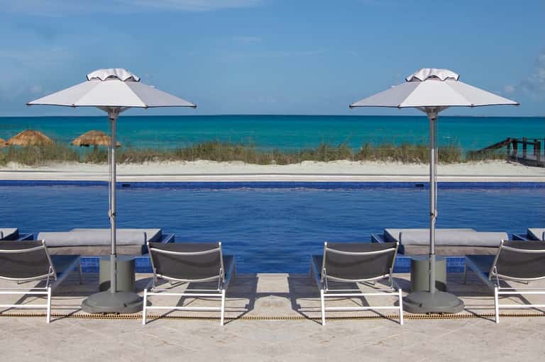 Beach resort pool overlooking turquoise ocean with white umbrellas and sandy beach