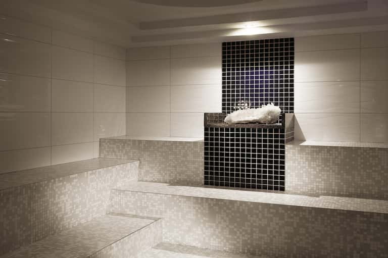 Luxurious spa room with multi-level white tiled benches and black tile accent wall