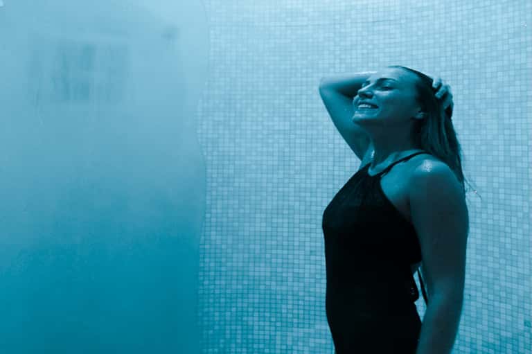 Woman swimming underwater in pool with blue mosaic tile walls and natural light