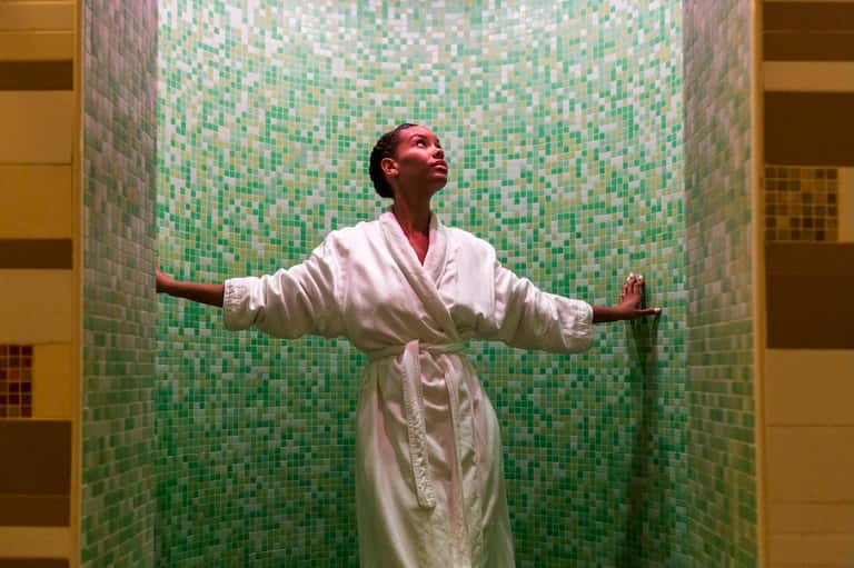 Woman in white robe relaxing in spa steam room with green mosaic tile walls