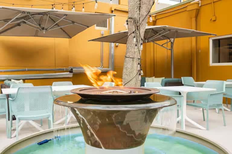Resort patio with fire pit, yellow walls, umbrellas, light blue chairs, and palm tree