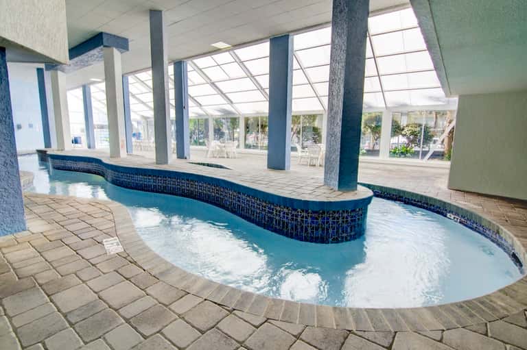 Indoor thermal pool with curved edges, blue tile accents, and skylight ceiling