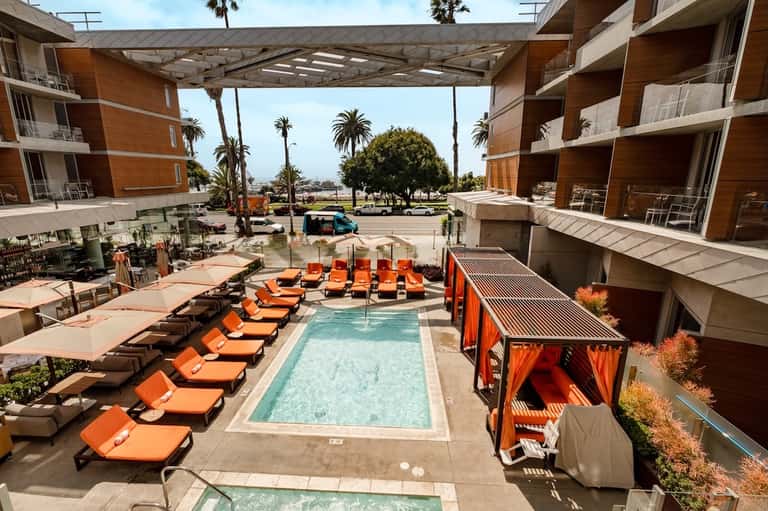 Resort courtyard pool with orange loungers, cabanas, and surrounding modern buildings