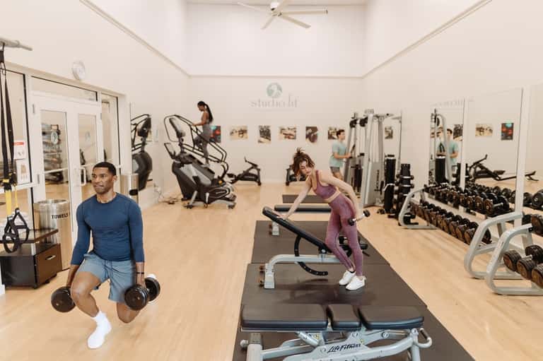 Bright fitness center with exercise equipment, mirrors, and people working out