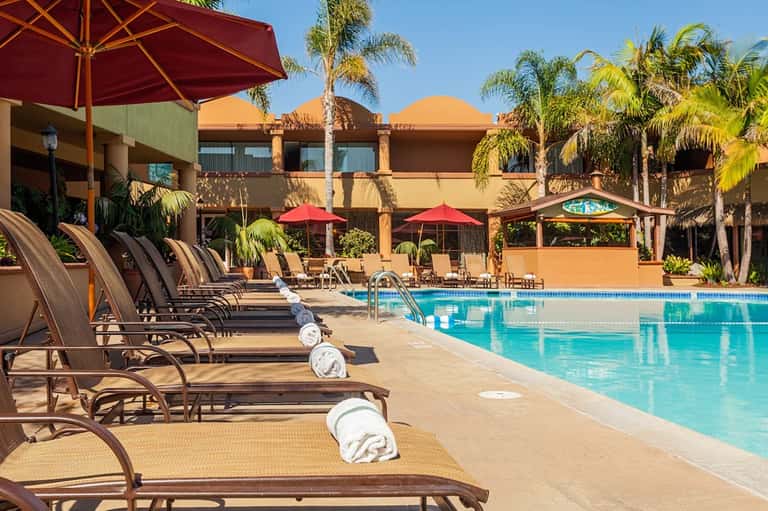 Resort pool area with lounge chairs, red umbrellas, desert landscaping, and southwestern architecture