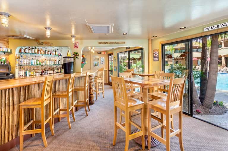 Casual beach bar with wooden furnishings, colorful wall display, and open doors to pool area