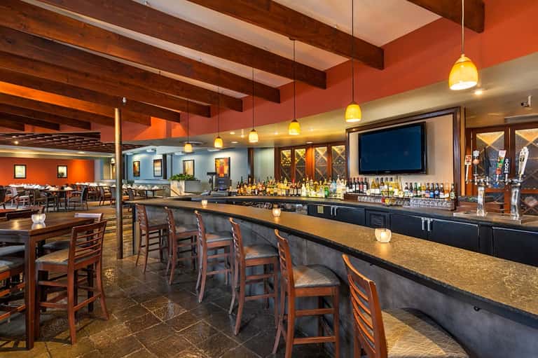 Spacious restaurant and bar with exposed wood beams, orange accent walls, pendant lighting, and dining area