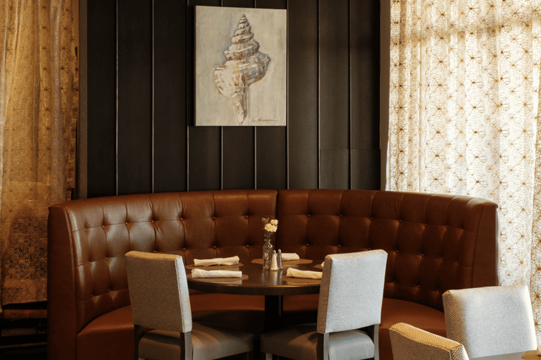 Intimate lounge seating with brown leather banquette, seashell artwork, and patterned wallpaper