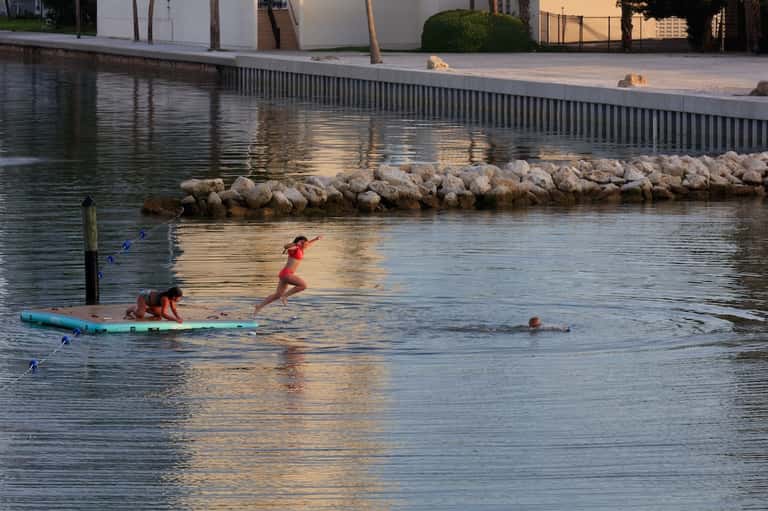 Waterfront lagoon with swimmers, paddleboarder, landscaped grounds, and modern residential buildings