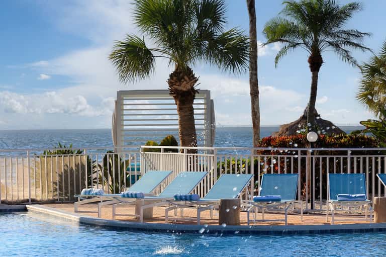 Beachfront resort pool overlooking the ocean with blue lounge chairs and palm trees