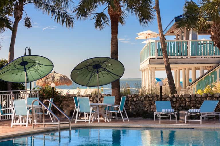 Beachfront pool area with green umbrellas, loungers, and ocean view through palm trees