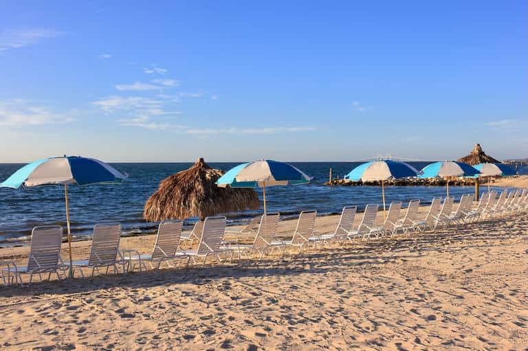 Beach lined with lounge chairs, blue and white umbrellas, and calm ocean view