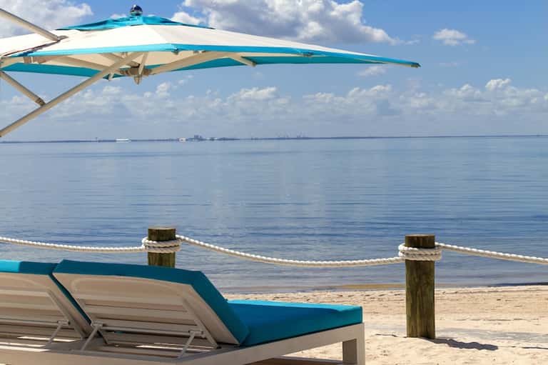 Turquoise cantilever umbrella and lounger on sandy beach with calm bay waters and horizon