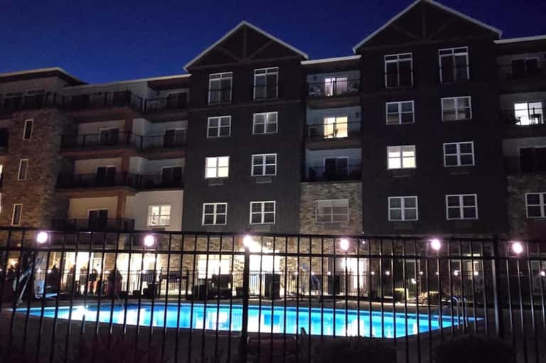 Apartment building exterior at night with lit windows and illuminated courtyard pool