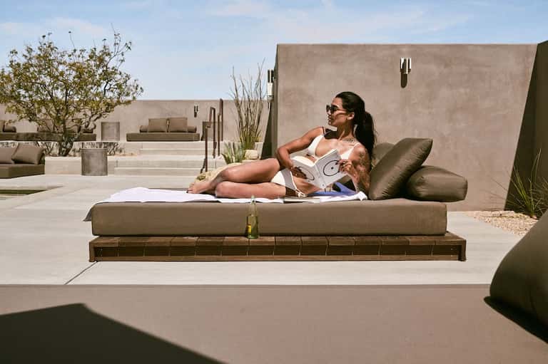 Woman relaxing on olive-green lounge chair on rooftop terrace with minimalist concrete design