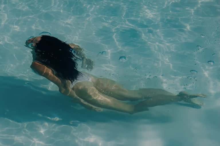 Person snorkeling in clear turquoise shallow water with visible fish and sun reflections
