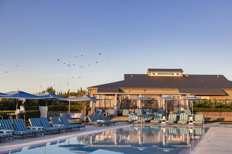Resort pool at dusk with striped loungers, blue cabanas, and main building reflected in water