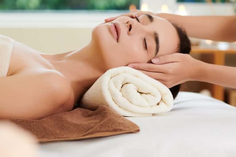 Spa massage treatment with relaxed client receiving facial massage from therapist's hands