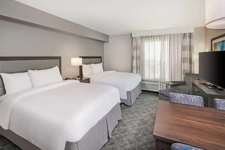 Hotel room with two queen beds, neutral décor, TV, and seating area