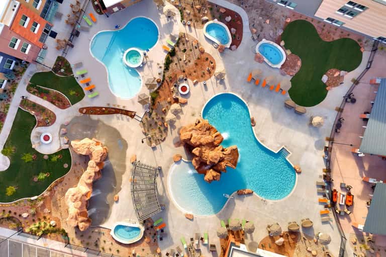 Aerial view of resort complex with multiple uniquely-shaped pools, landscaping, and surrounding buildings