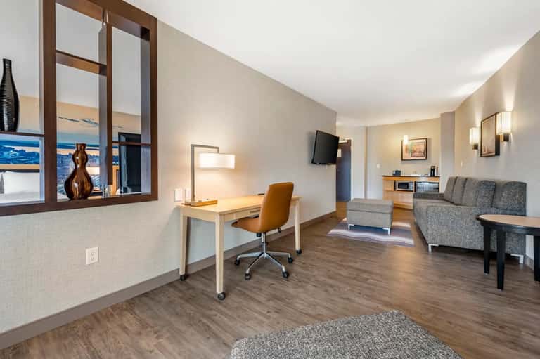 Modern hotel suite with ocean view window, work desk, comfortable seating area, and contemporary décor