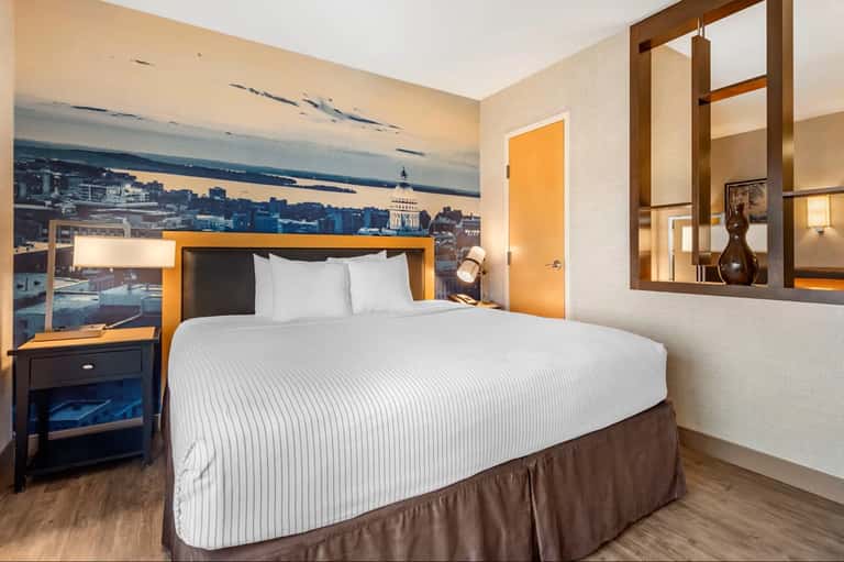 Modern hotel bedroom with orange accents, cityscape wall mural, and contemporary furnishings