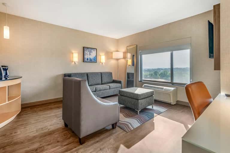 Hotel suite with gray sofa, armchair, window seating, and landscape view of countryside