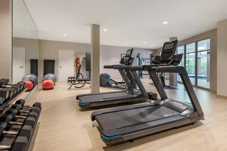Fitness center with treadmills, exercise equipment, mirrors, and large windows overlooking grounds
