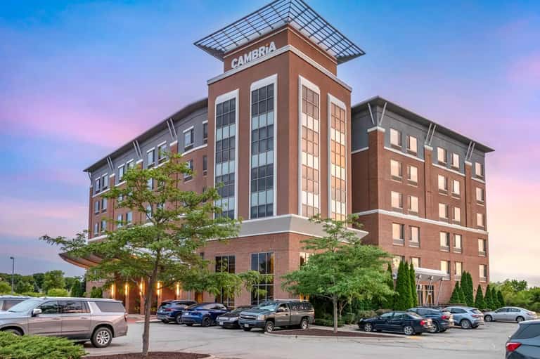 Cambria Hotel exterior at dusk with brick facade, illuminated windows, parking lot, and landscaping