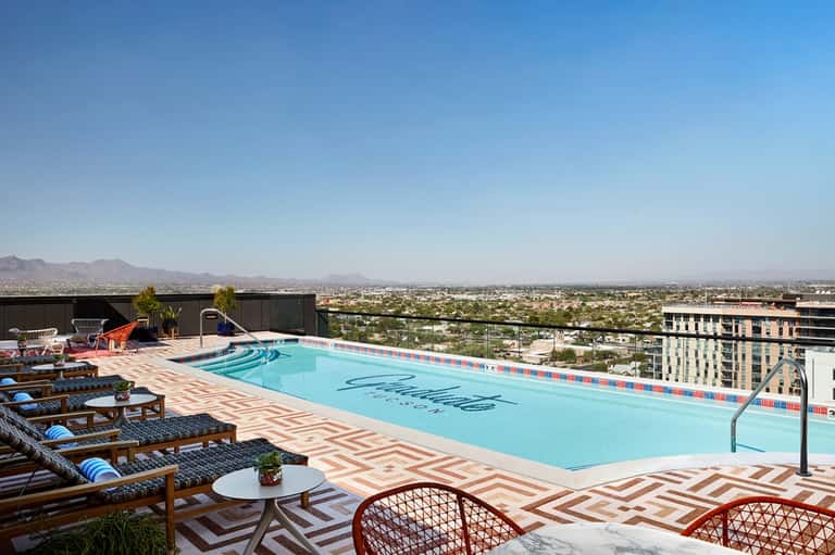 Rooftop pool with geometric patterned deck, lounge chairs, and distant desert mountain landscape view
