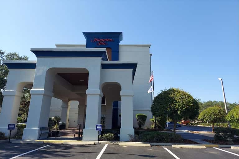 Hamilton Inn hotel exterior with white columned entrance and manicured hedges under blue sky