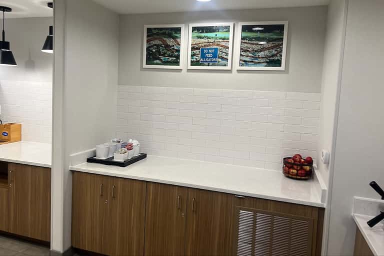 Hotel pantry nook with white subway tile, wood cabinetry, and alligator-themed artwork
