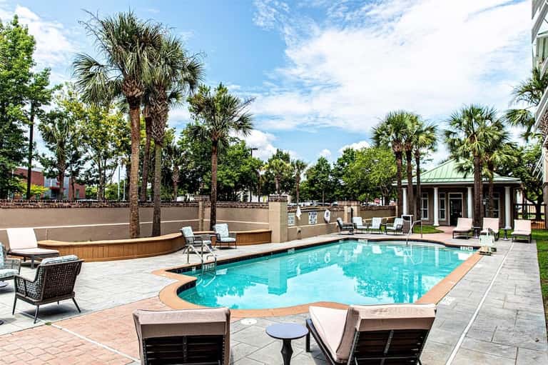 Resort pool surrounded by palm trees, lounge chairs, and modern building architecture