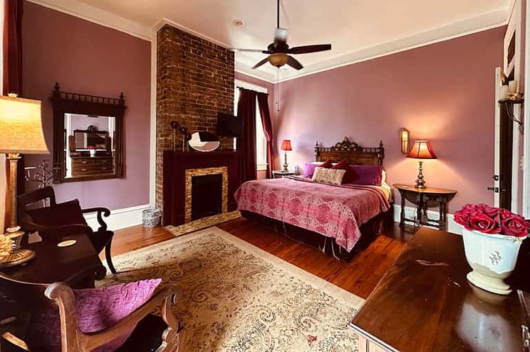 Elegant bedroom with mauve walls, fireplace, ornate wooden bed, and decorative furnishings