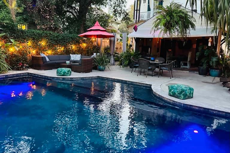 Backyard pool at night with blue LED lighting, lounge seating, and garden landscaping