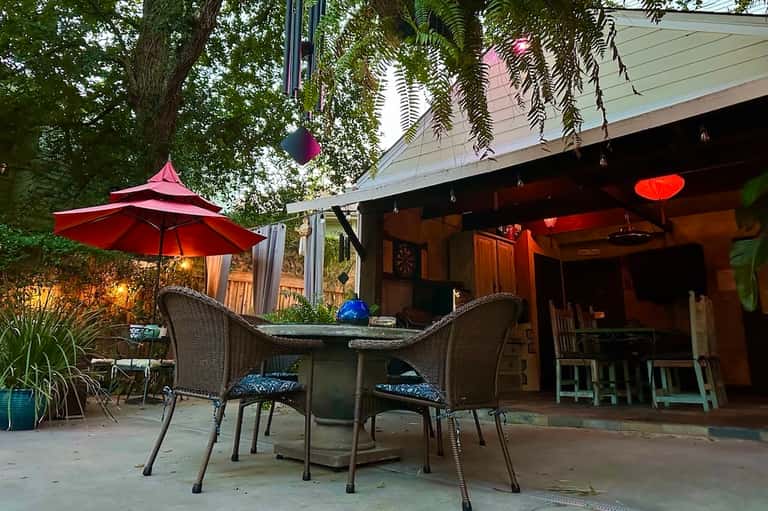 Outdoor patio area under pergola with red umbrella, wicker lounge chairs, and warm ambient lighting