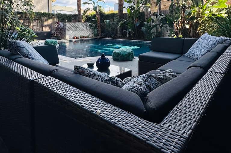 Modern backyard pool surrounded by tropical plants, black lounge furniture, and stone decking