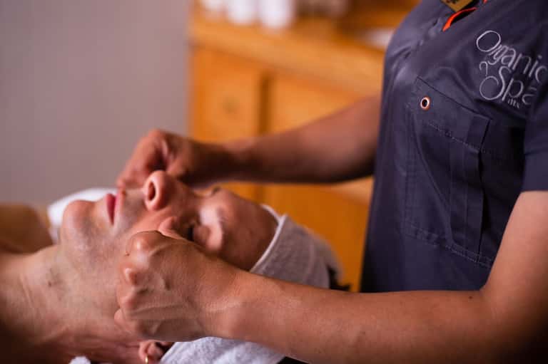 Spa therapist performing facial massage on male guest in wellness treatment room