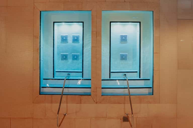 Two rectangular windows showing indoor swimming pool with underwater jets and lounge chairs