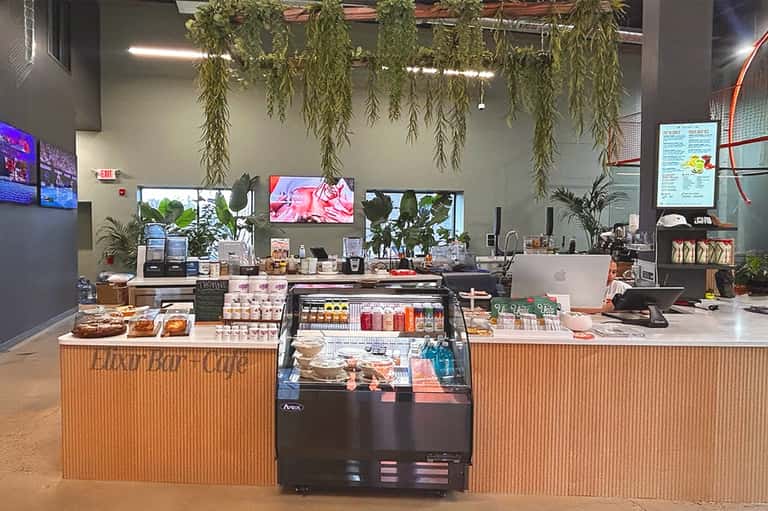 Bright café counter with plants, pastries display, and menu boards on walls