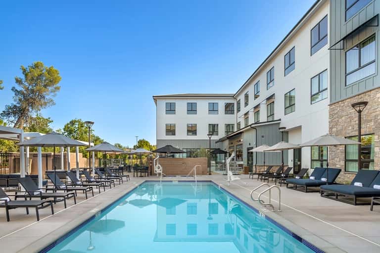 Hotel courtyard pool with lounge chairs, umbrellas, and modern building exterior