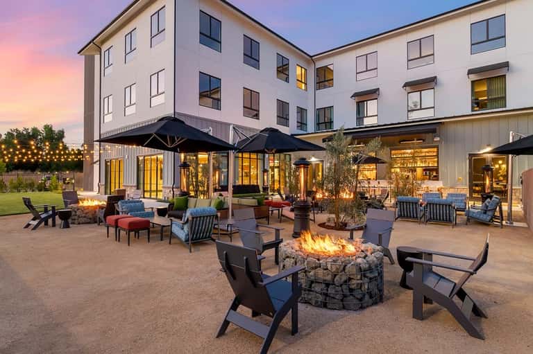 Outdoor courtyard at dusk with firepit, lounge chairs, umbrellas, and illuminated hotel building