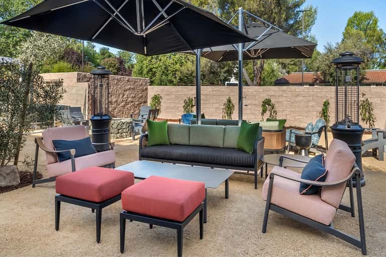 Outdoor lounge area with colorful furniture, large black umbrellas, fire pits, and brick walls