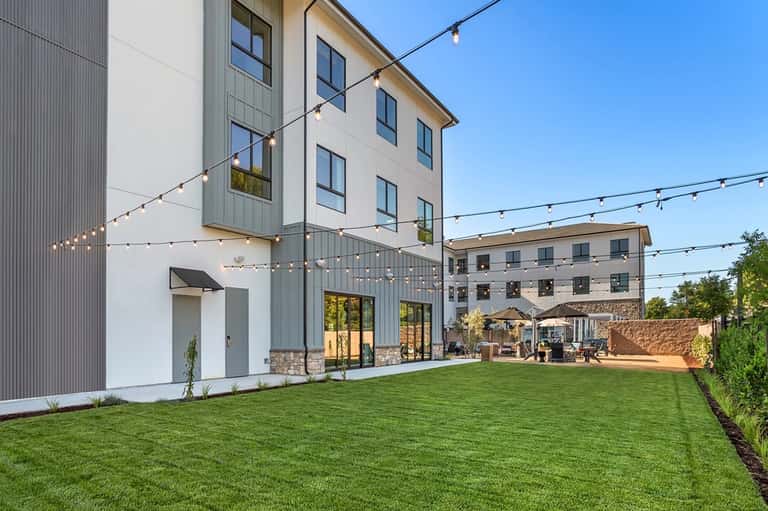 Modern residential courtyard with manicured lawn, string lights, contemporary architecture, and patio furniture