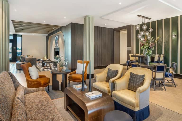 Modern hotel lobby lounge with gold velvet chairs, green accent wall, pendant lights, and wood elements