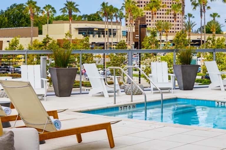 Resort rooftop pool deck with modern loungers and large planters overlooking palm trees and cityscape